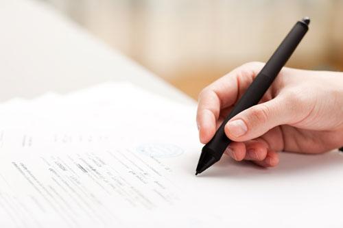 Bilde av en hånd som holder en sort penn og skriver på et skjema